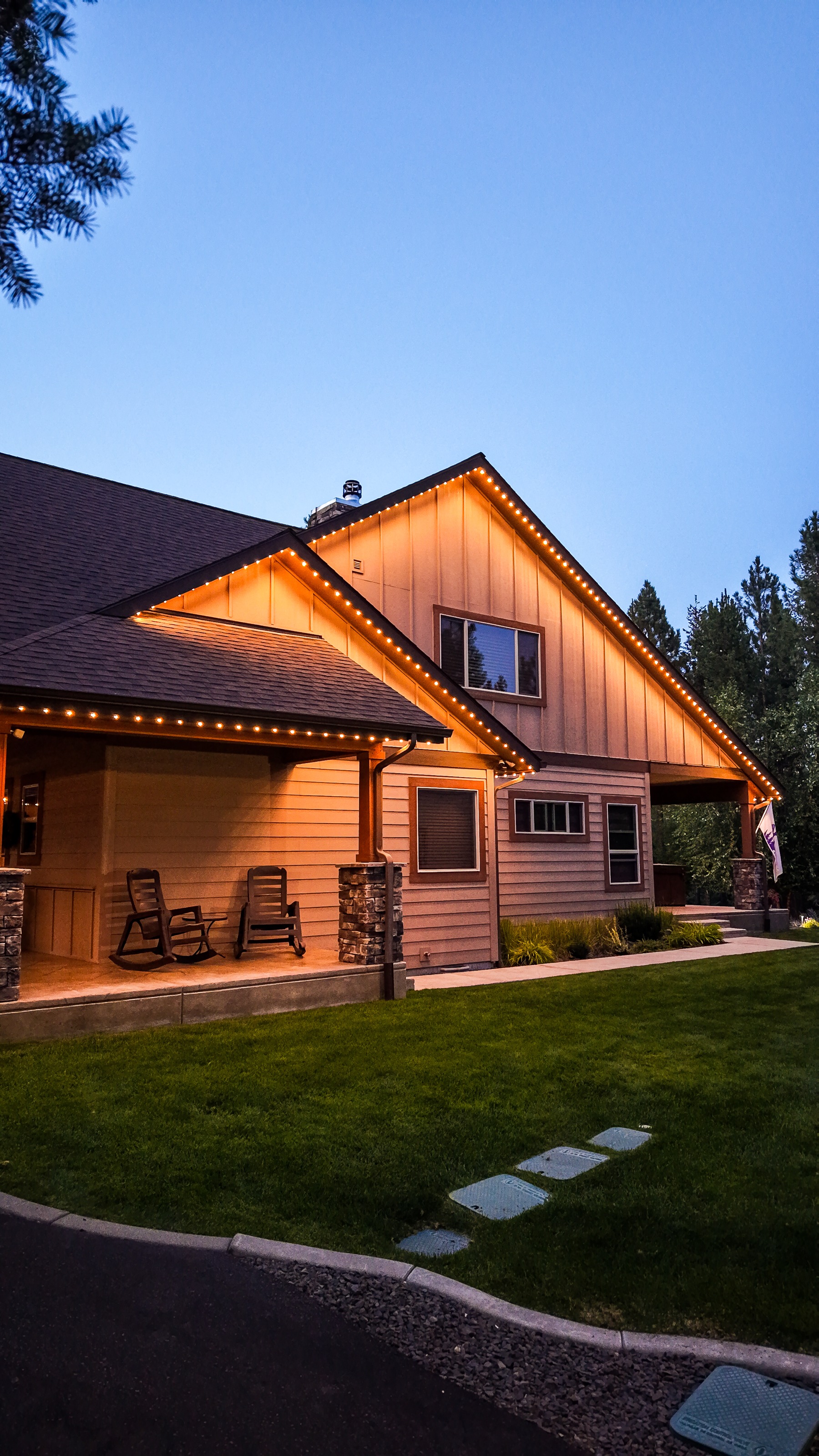 A craftsman home's front porch and gable lit with warm white trim lighting at dusk