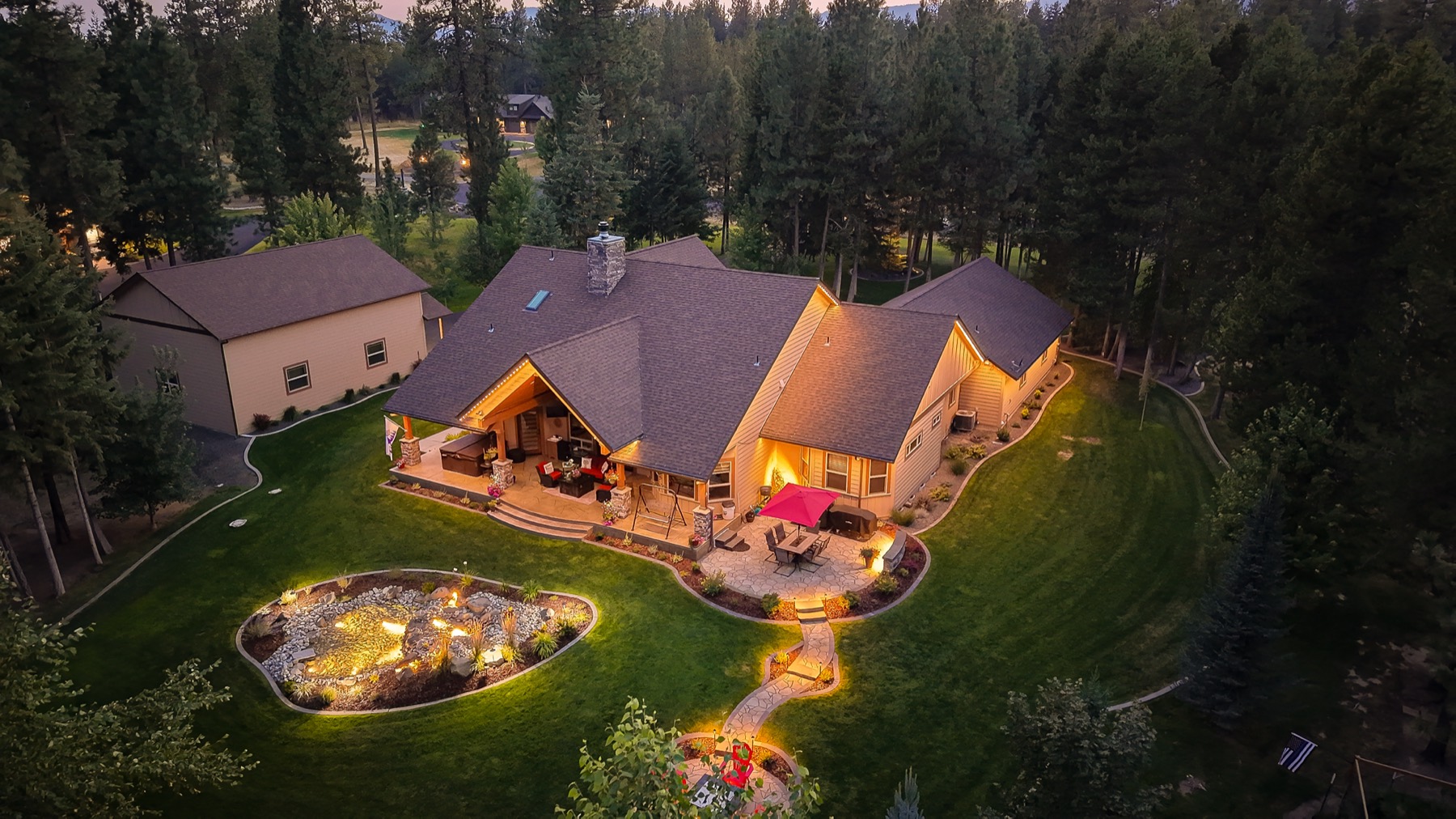 Aerial view of a home's roofline and backyard lit with warm white trim lighting at dusk
