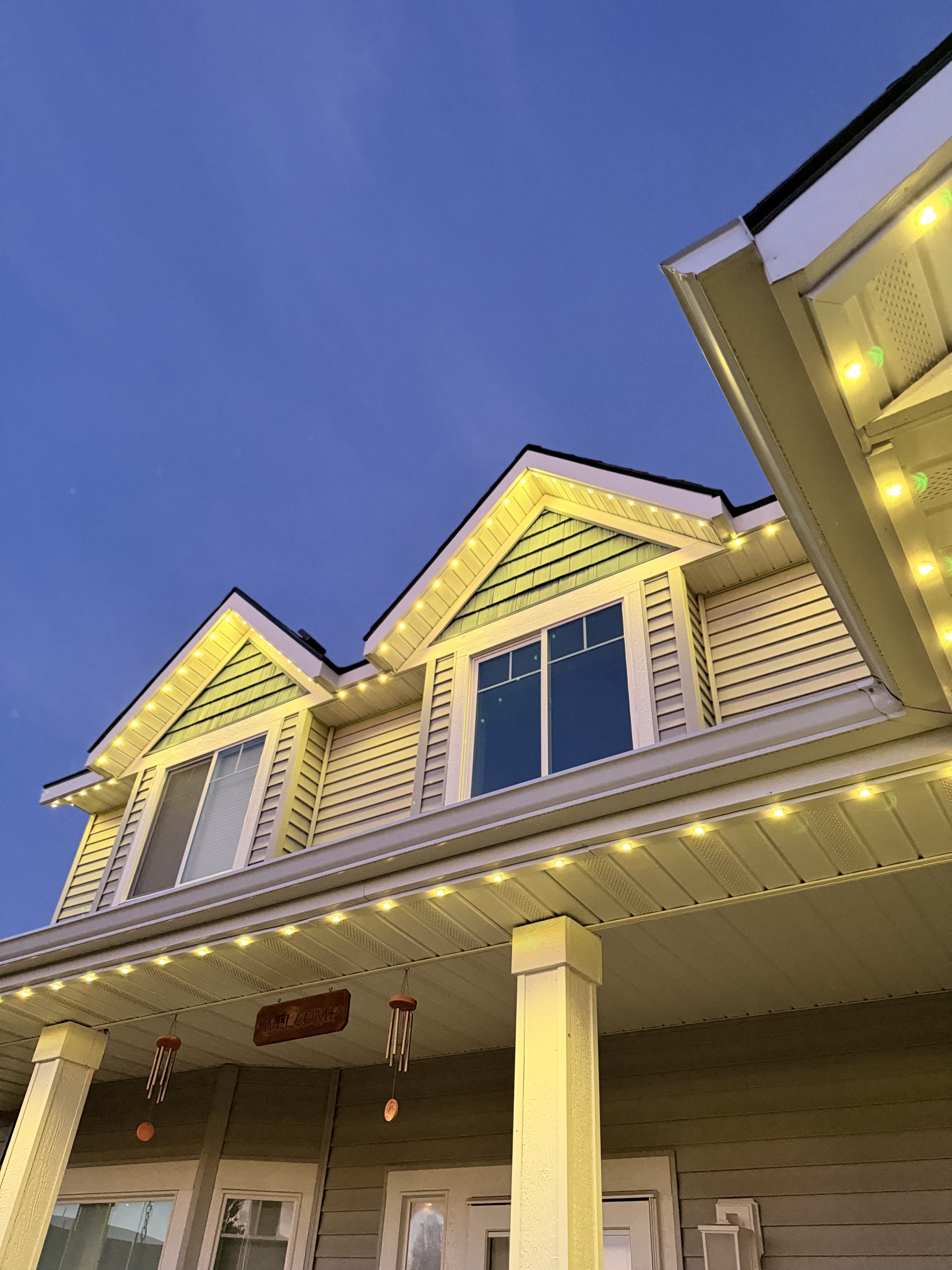 Close-up of a home's gables and porch lit with warm white trim lighting at dusk