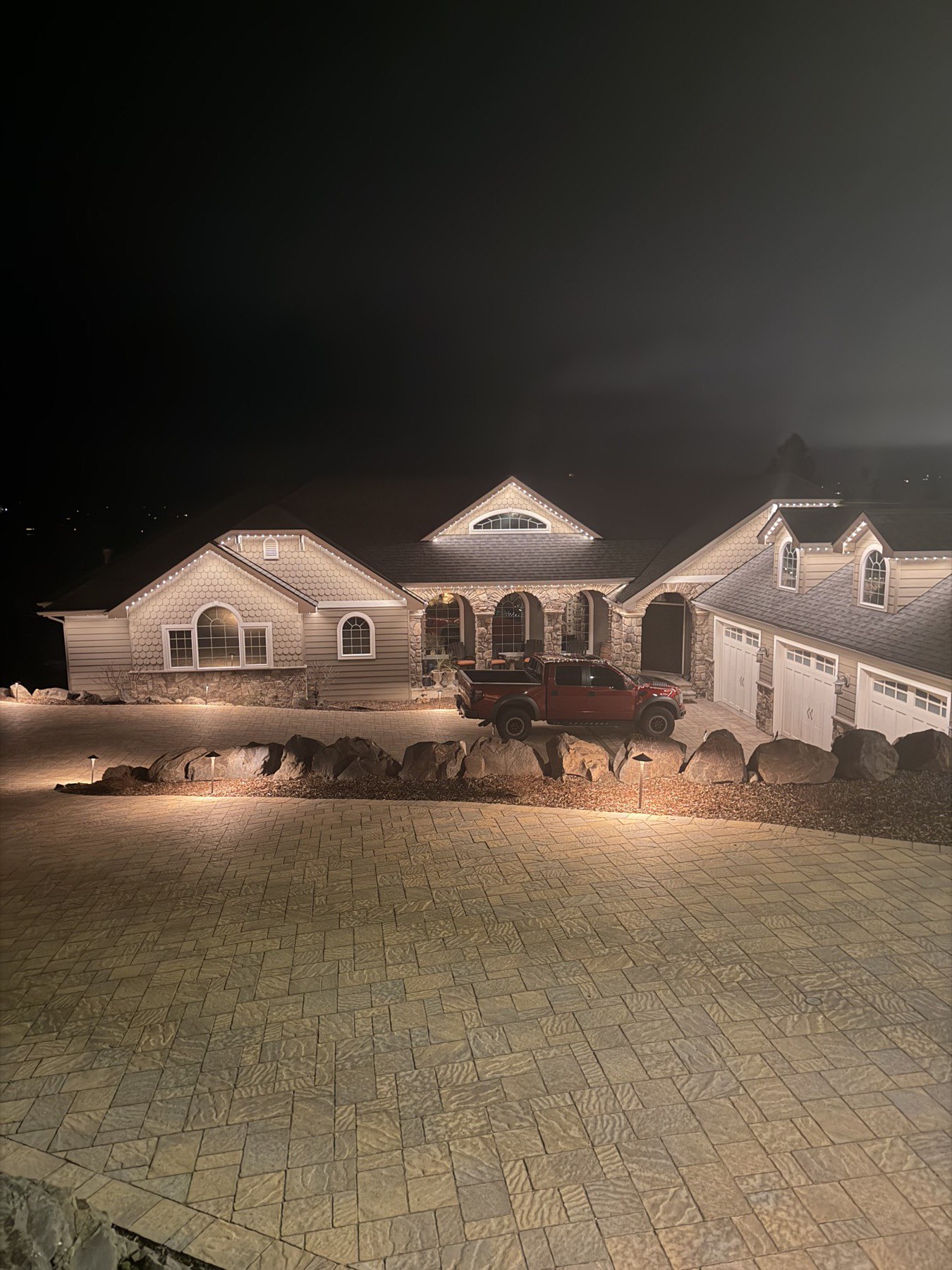 A home's entrance and driveway lit with warm white trim lighting at dusk