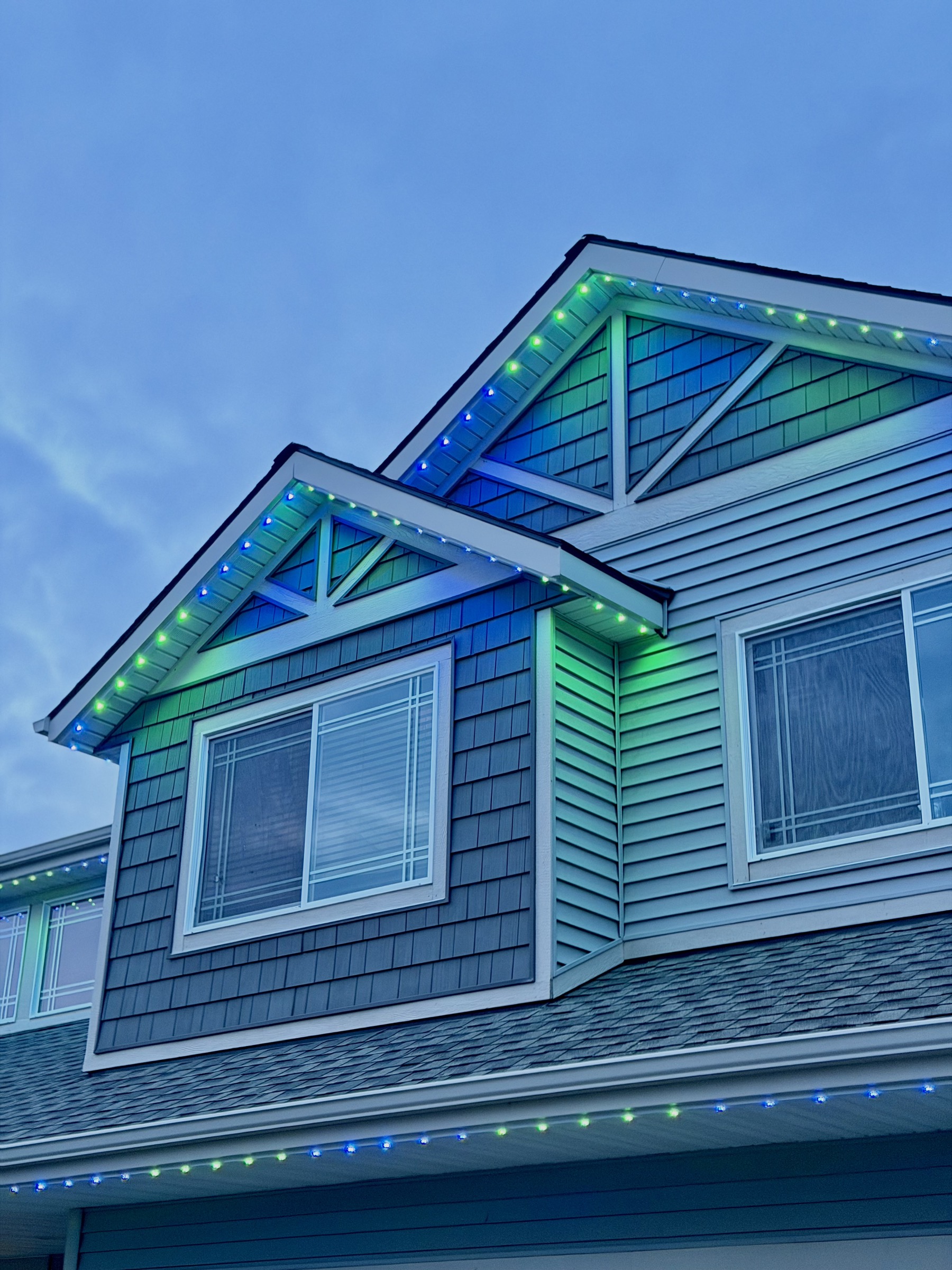 Close-up of a home's gable lit in blue and green trim lighting at dusk