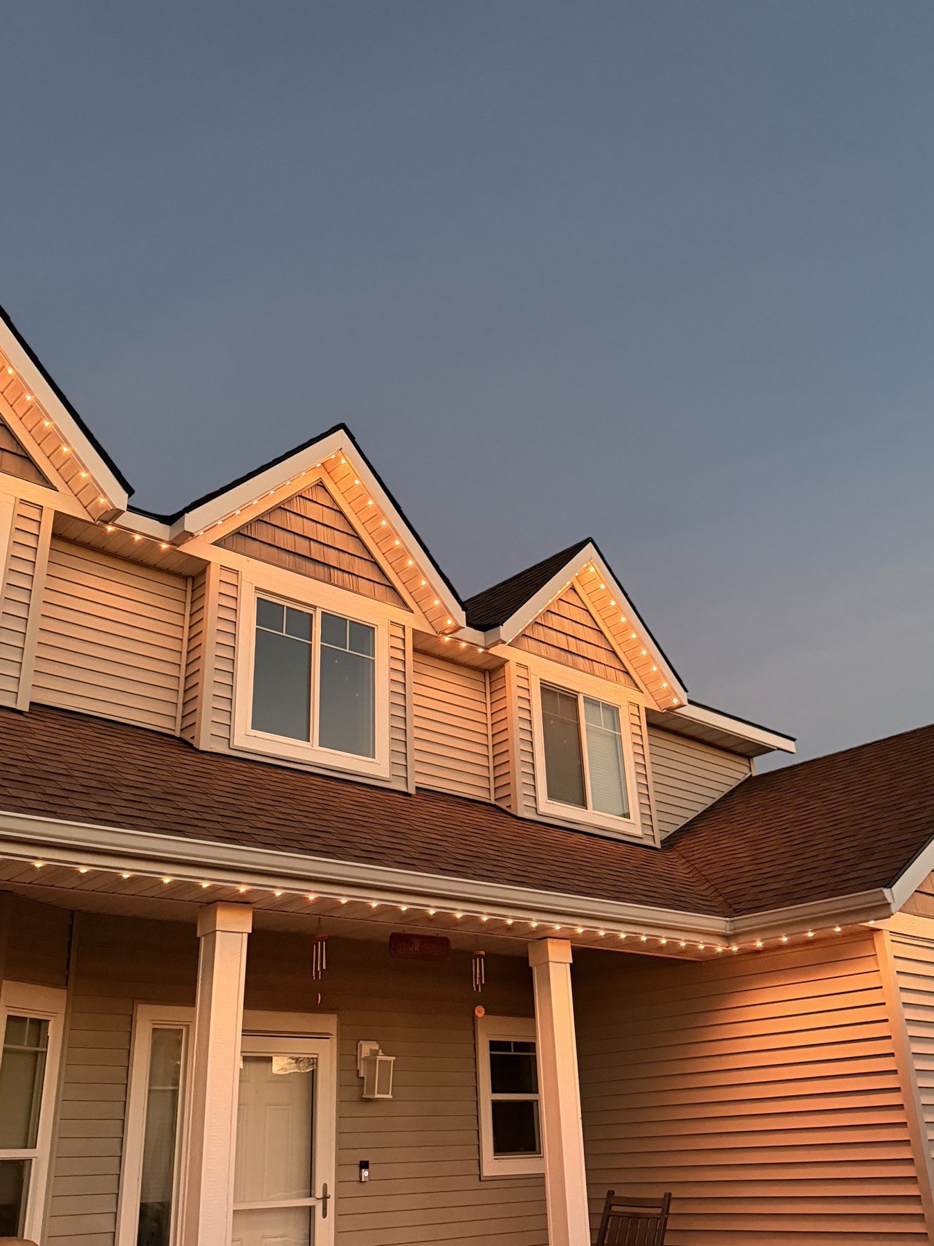 Close-up of a home's gables and porch lit with warm white trim lighting at dusk