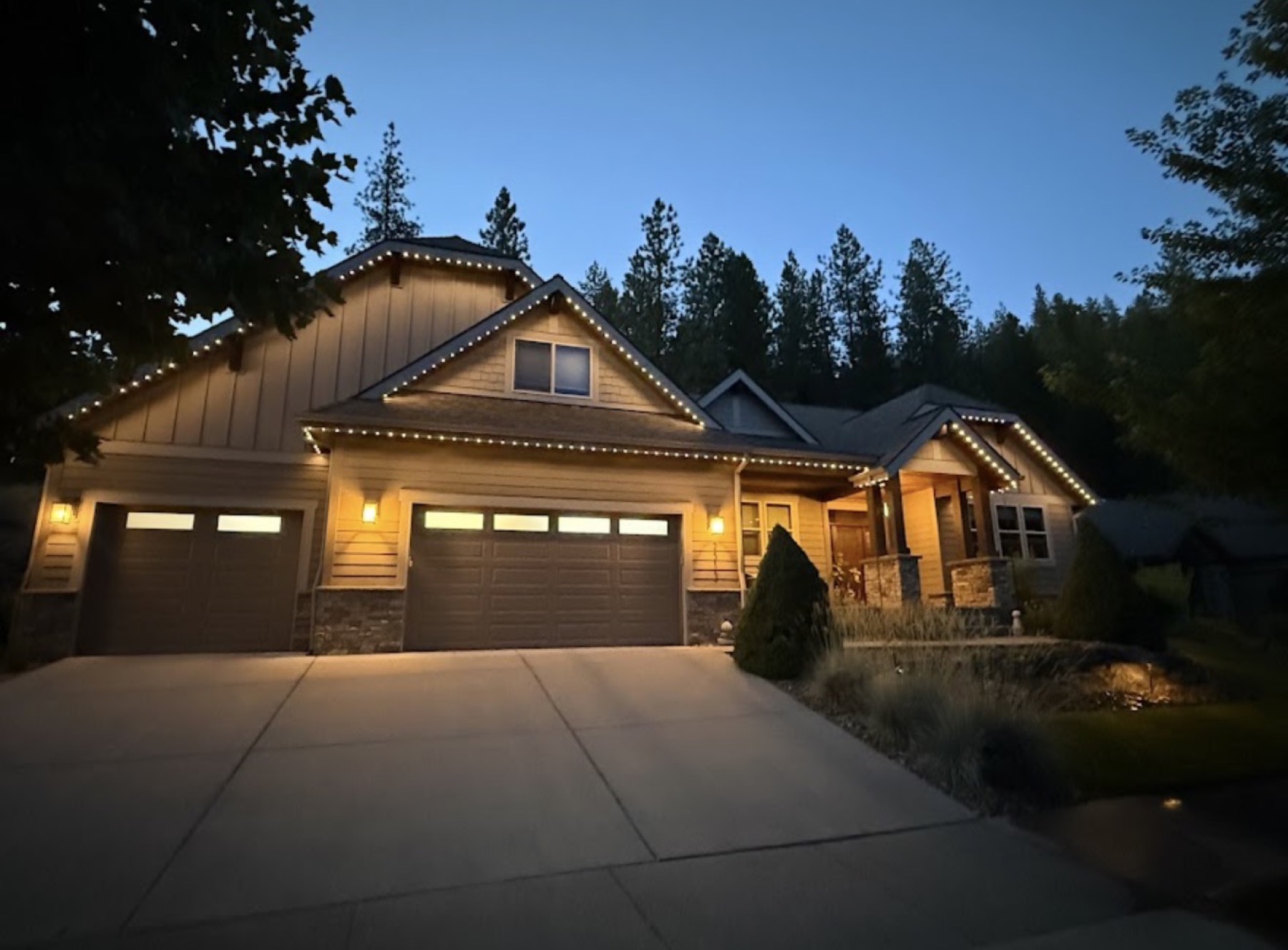A home's driveway and entrance lit with warm white trim lighting at dusk