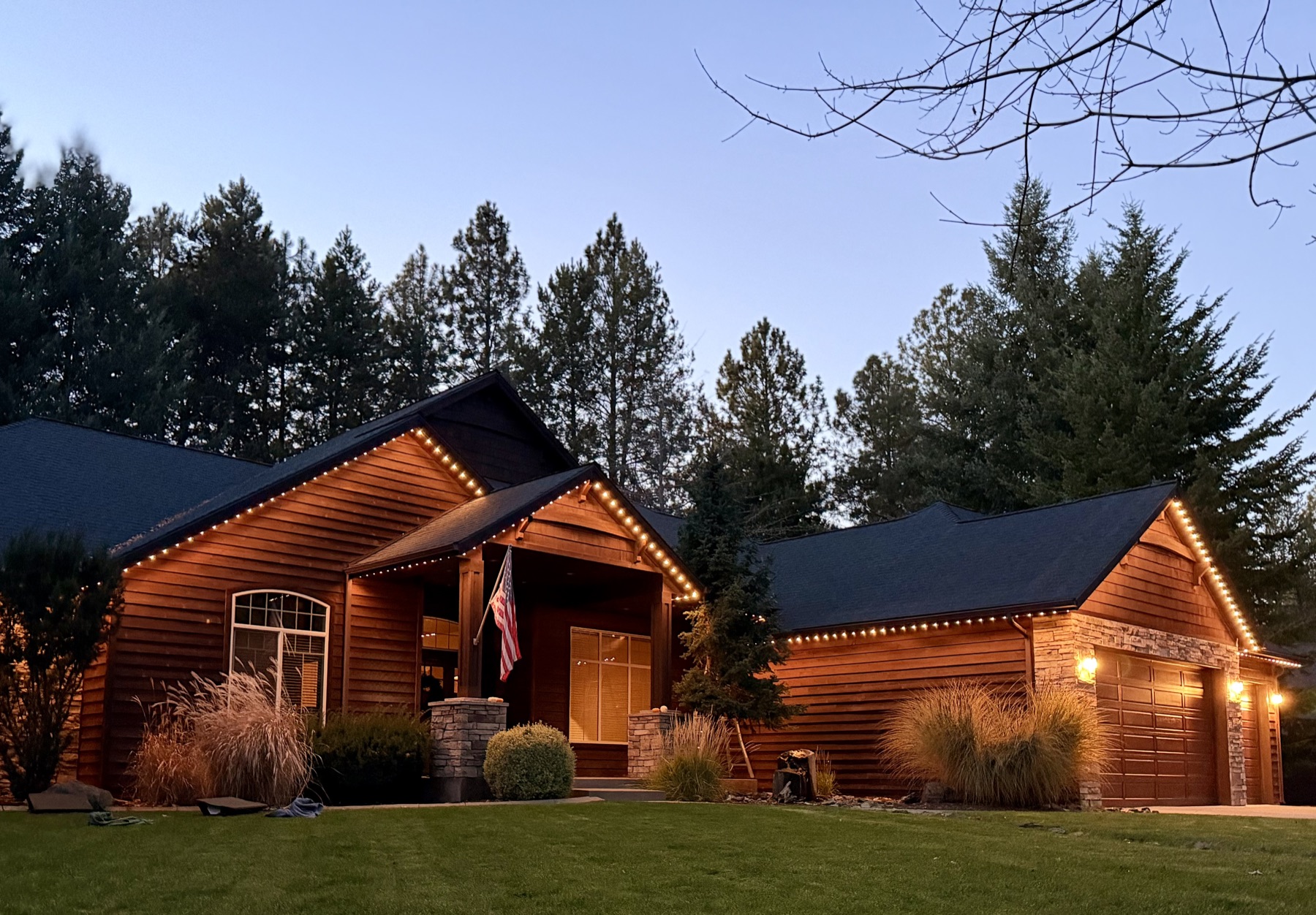 A log home's gables lit with warm white trim lighting at dusk