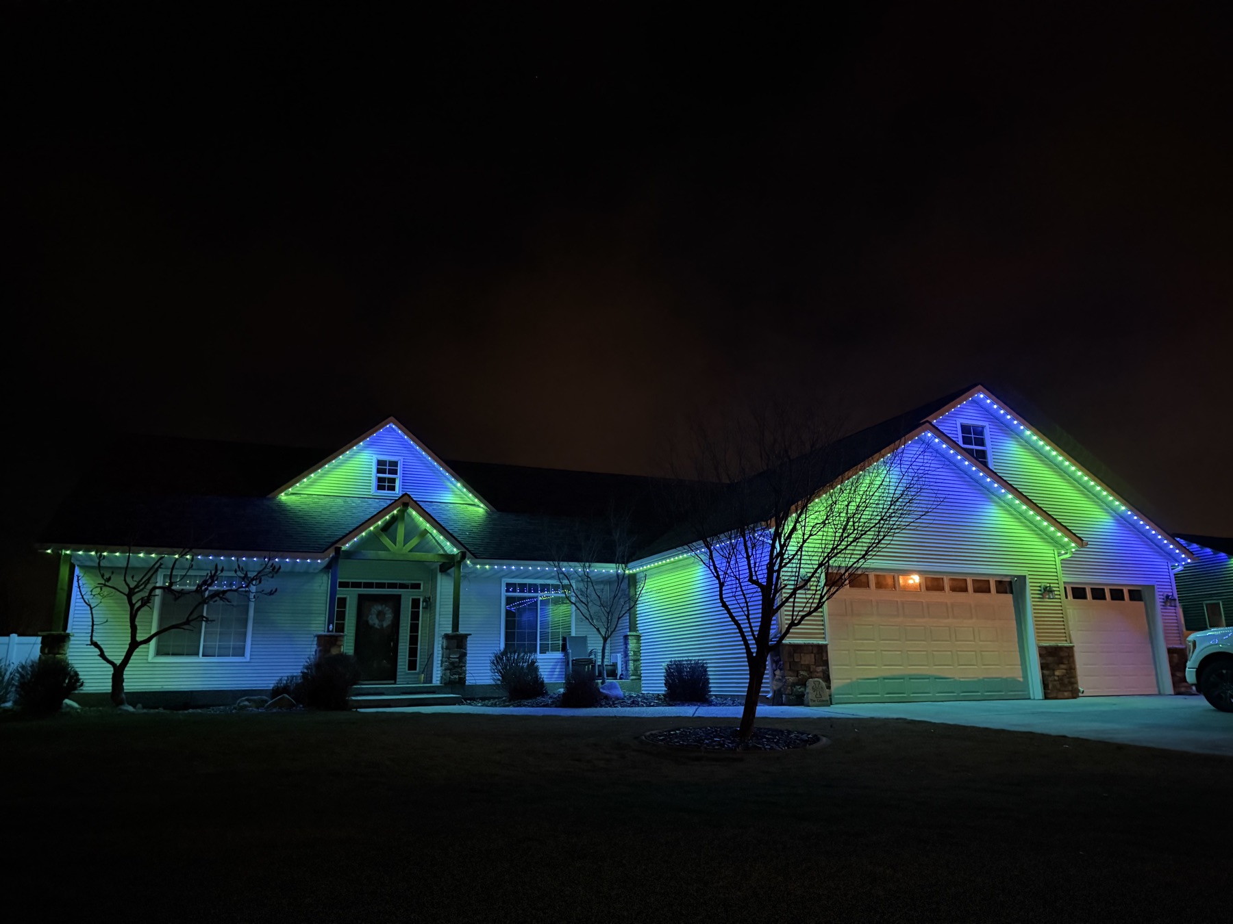 A home's roofline lit in green and blue team-color trim lighting at night